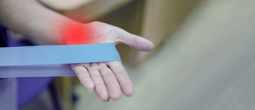 foto di una mano con una fascia per esercizi, con una parte evidenziata di rosso, ad indicare zona di dolore