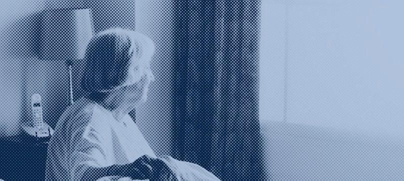 immagine a due colori che rappresenta una donna anziana seduta su un letto, che guarda verso una finestra