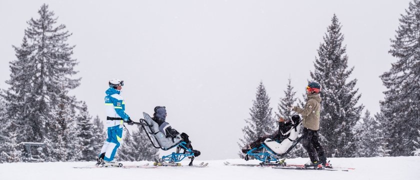 due maestri di sci sulle piste uno difonte all'altro: davanti a ciascuno, un utente sul dualski