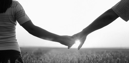una coppia si tiene la mano in un campo di grano e guarda verso il sole, verso il futuro